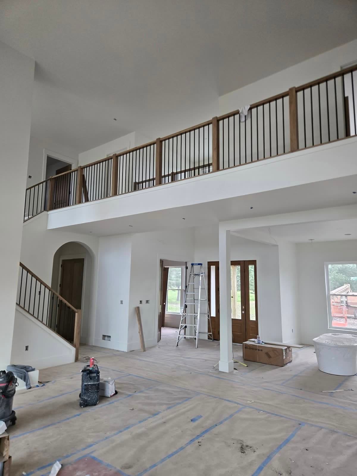 Two-storey great room with a balcony railing, floors covered and the room prepped for painting